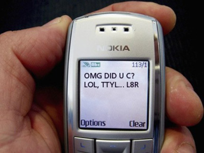 Hand holding a mobile phone showing a text message written in abbreviations